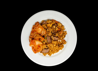 Homemade fried rice with sliced grilled lamb and kimchi on a white plate, isolated on black background. Top view or flat lay.