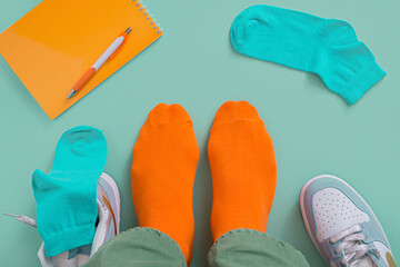Feet of a man in orange socks and green jeans. Teal background with notepad and pen