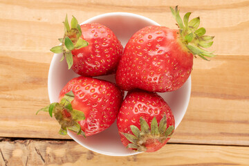 Several sweet strawberries with white ceramic saucer on wooden table, macro, top view.