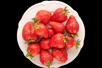 Several red sweet strawberries with white ceramic dish on black background, macro, top view.
