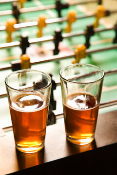 Two glasses of beer on foosball table.