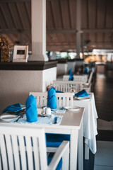 Maldives; Selective focus on nicely decorated dining tables with blue folded napkins, silverware, and a blue sous plat, highlighting the attention to detail and sophistication of the setting.