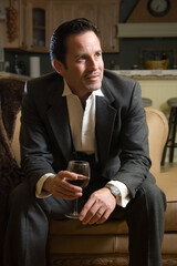 Man in a business suit sitting on the sofa drinking a glass of red wine