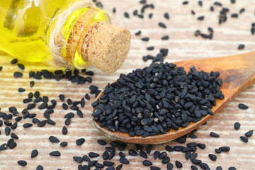 Black cumin seeds and essential oil with bowl and wooden shovel or spoon. Nigella Sativa in glass bottle. Organic herbal medicine for many diseases