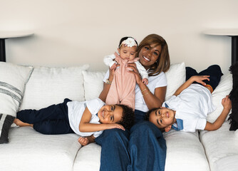 Beautiful African American woman lifting her baby girl; her six year old twin boys sprawling in playful poses next to her - obrazy, fototapety, plakaty