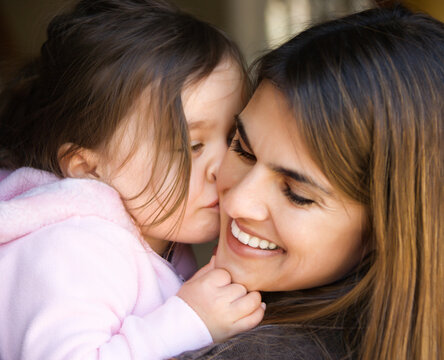 Caucasian mother holding daughter kissing her cheek and smiling.