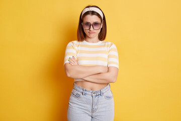 Offended unhappy woman wearing striped T-shirt hair band and sunglasses standing isolated over...