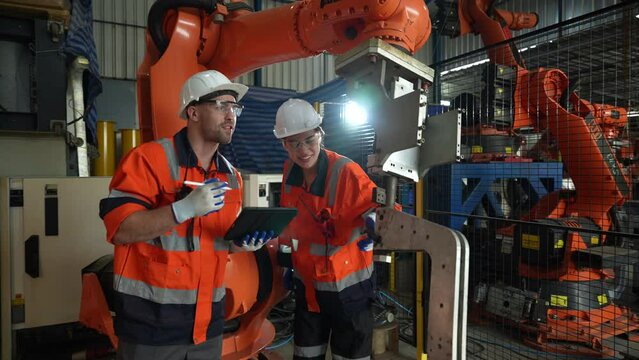 Team of engineers in an industrial factory enter commands and test the operation of the mechanical arm.