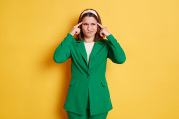 Sad woman wearing green jacket standing isolated over yellow background thinking trying to remember...