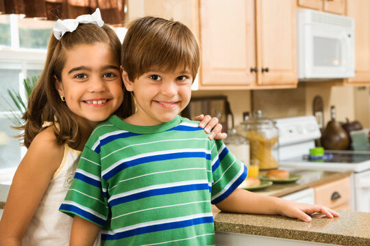 Hispanic children in kitchen smiling at viewer.