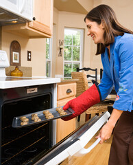 Side view of Hispanic mid adult woman putting cookies into oven.