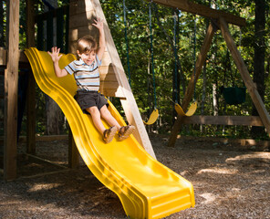 Hispanic boy sliding down outdoor slide with arms raised above head.