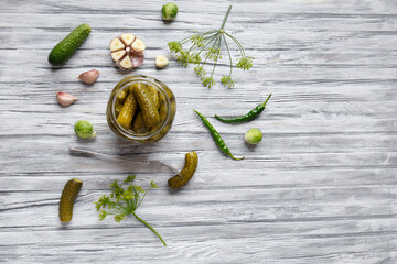 Pickled cucumbers in an open jar, gherkin on a fork and garlic on a light wooden background, top view, copy space. Homemade canned cucumbers.