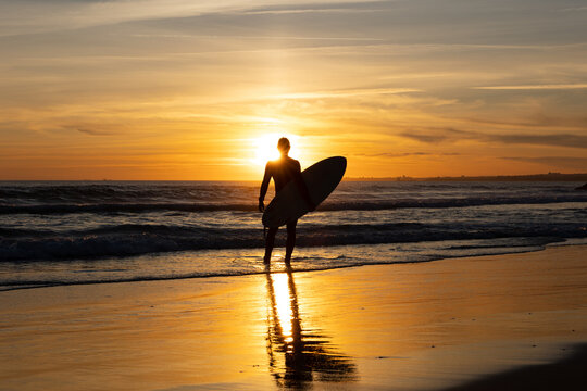 Silhouette of a man surfer holding surfboard standing alone on the seashore