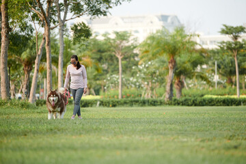 Naklejka na ściany i meble Woman walking in summer park with big fluffy dog