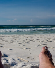 Fototapeta na wymiar Man's foot on beach chair with beach and ocean in background.