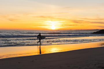 Fototapeta na wymiar A man surfer running on the seashore at bright orange sunset
