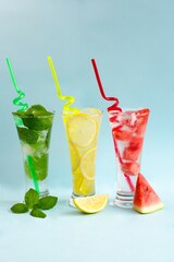 Three glasses of chilled drinks on a blue background, lemonade, watermelon lemonade, mint lemonade, iced drinks