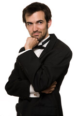 Attractive young brunette man with a beard wearing a black tuxedo posing with hand on chin