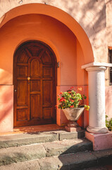 Fototapeta na wymiar Elegant entryway: a neoclassical wood door, arches and pillars, in pastel color building under warm sunlight