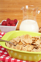A bowl of cornflakes, milk and raspberries on bamboo mat