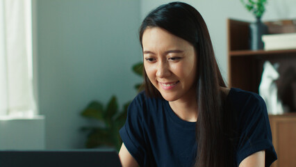 Beautiful young asian woman looking at screen, using laptop browsing the internet. Happy focused attractive lady typing laptop computer sits at desk in living room working online remotely from home