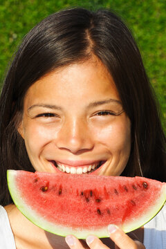 Beautiful woman smiling while eating watermelon outdoors on a hot summer day