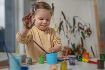 One toddler girl with colouring hands, playing with painting tools and paint with colours, early child education and development, creativity concept 