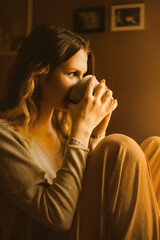A  contented lady, clad in soft beige loungewear, savoring a cup of coffee in kitchen as the day...