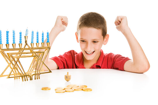 Cute little boy on Chanukah playing with his dreidel.  Isolated on white with menorah and gelt.