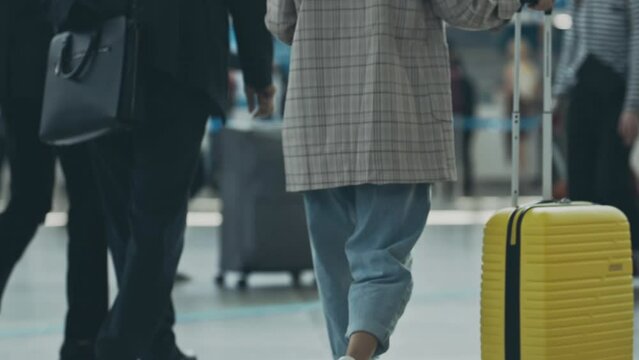 View from back of young businesslady moving towards registration stand. Young woman slowly walking in airport terminal with suitcase. Girl preparing to departure for working trip. Concept of travel.
