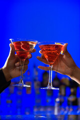 African-American hands toast martini glasses against a bright blue background. Vertical shot.
