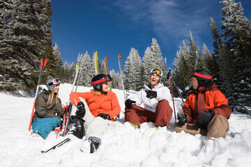 Group of male and female skiers sitting in the snow relaxing talking and smiling. Horizontal shot.