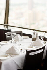 High angle view of a restaurant table with place settings and a white tablecloth.  The table is by a window. Vertical shot.