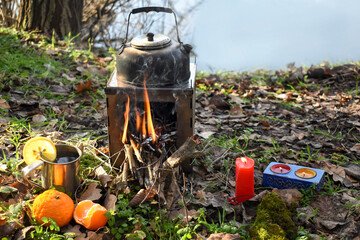 Kettle on a wood burning stove, a cup of tea with a slice of lemon, tangerines and candles, a picnic in nature