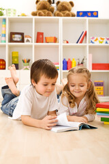 Fototapeta premium Little sister let me show you how to read - kids with books laying on the floor
