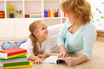 Fototapeta premium Story time with mom - little girl and woman reading laying on the floor