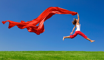 Beautiful young woman jumping on  a green meadow with a colored tissue