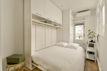 a bedroom with a bed and white cupboards on the wall next to the bed is a green chair in front of it