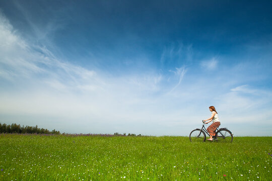 Happy young woman on a green meadow riding a bicycle