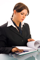 a young woman in black jacket and white shirt and a tie sitting down behind an office table and playing with glasses