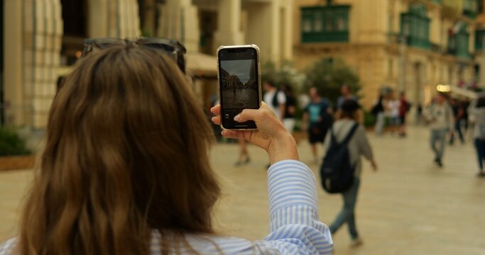 Tourist female student press shutter button in camera app on phone in street. View of smartphone screen while unrecognizable young woman takes photo in old downtown.