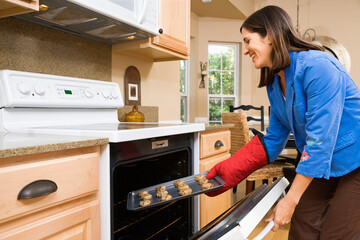 Fototapeta na wymiar Side view of Hispanic mid adult woman putting cookies into oven.