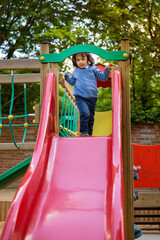Handsome active little boy having fun while playing and sliding on the outdoor playground. Kids...