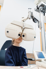Child looks into phoropter during an eye examination of pediatric ophthalmologist. Phoropter for measuring refractive error and determining information for prescription for eyeglasses.
