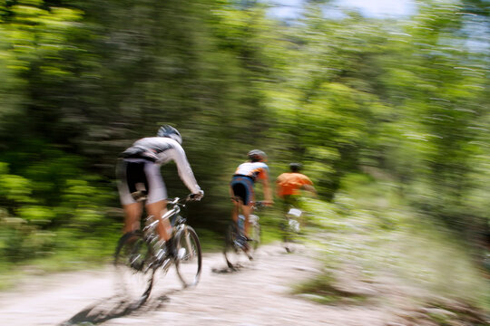 Blurred panning shot of three mountain bikers riding through the forest.
