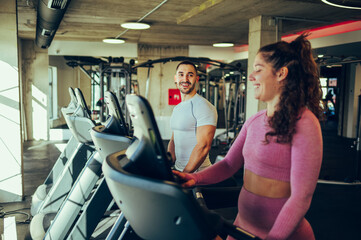 The healthy sporty couple is walking on a treadmill in a gym.