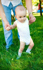 Baby boy walking in grass with fathers help