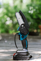mini portable electric chain saw on summer garden background 