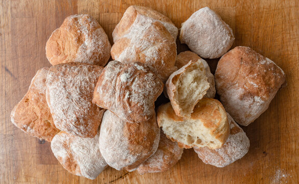 A pile of freshly baked ciabatta white crusty home-made rolls on a rustic wooden table, Top view, Side view.